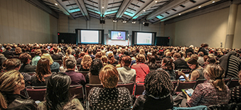 Vue arrière de milliers de personnes qui écoutent un conférencier à la conférence Transformation Qualité de la santé, l'événement vedette de Qualité des services de santé Ontario.