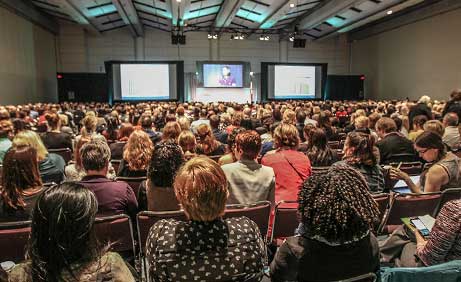Vue arrière de milliers de personnes qui écoutent un conférencier à la conférence Transformation Qualité de la santé, l'événement vedette de Qualité des services de santé Ontario.