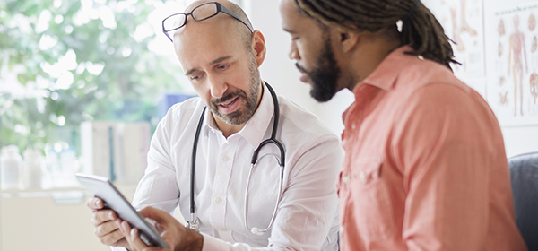 Male doctor looking at IPad with male patient