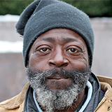 An elderly man in a hat looking at the camera