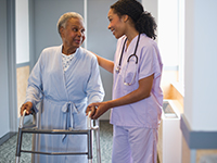 A nurse assists an older patient using a walker