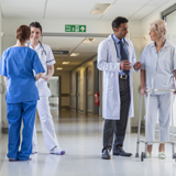 A doctor speaking to a patient with a walker and two health care providers speaking to each other in the hall of a hospital