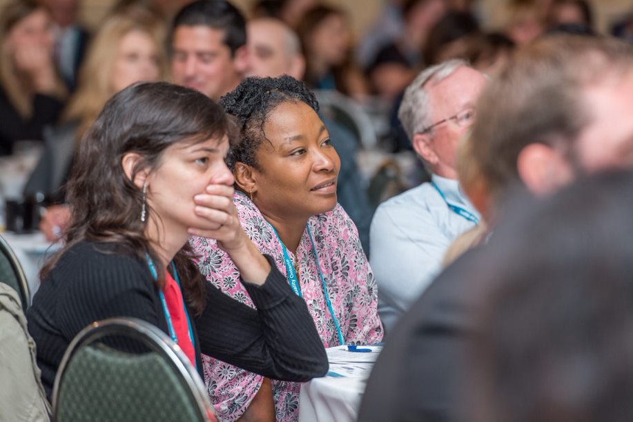 Des participants au Sommet, assis à une table, écoutent attentivement la conférence.