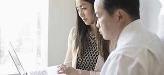 Une femme et un homme qui consultent des documents à l’ordinateur