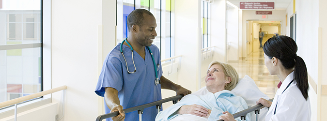 doctor and nurse talk with a patient lying on a hospital gurney in a hallway