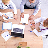 A bird's eye view of four doctors working together to improve health quality around a table.